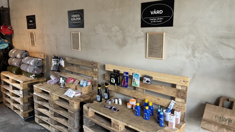 Butikshyllor av lastpallar med hundvårdsprodukter under skyltarna Vård och Första hjälpen.