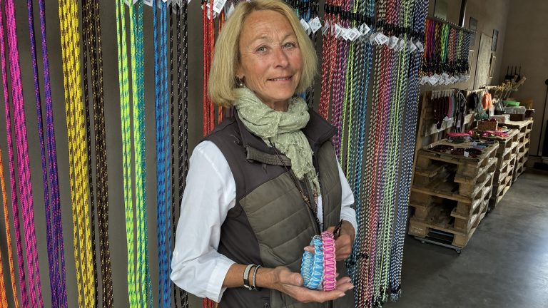 Petronella Lindmark håller upp ett flätat hundkoppel framför butikens vägg av koppel i olika färger.